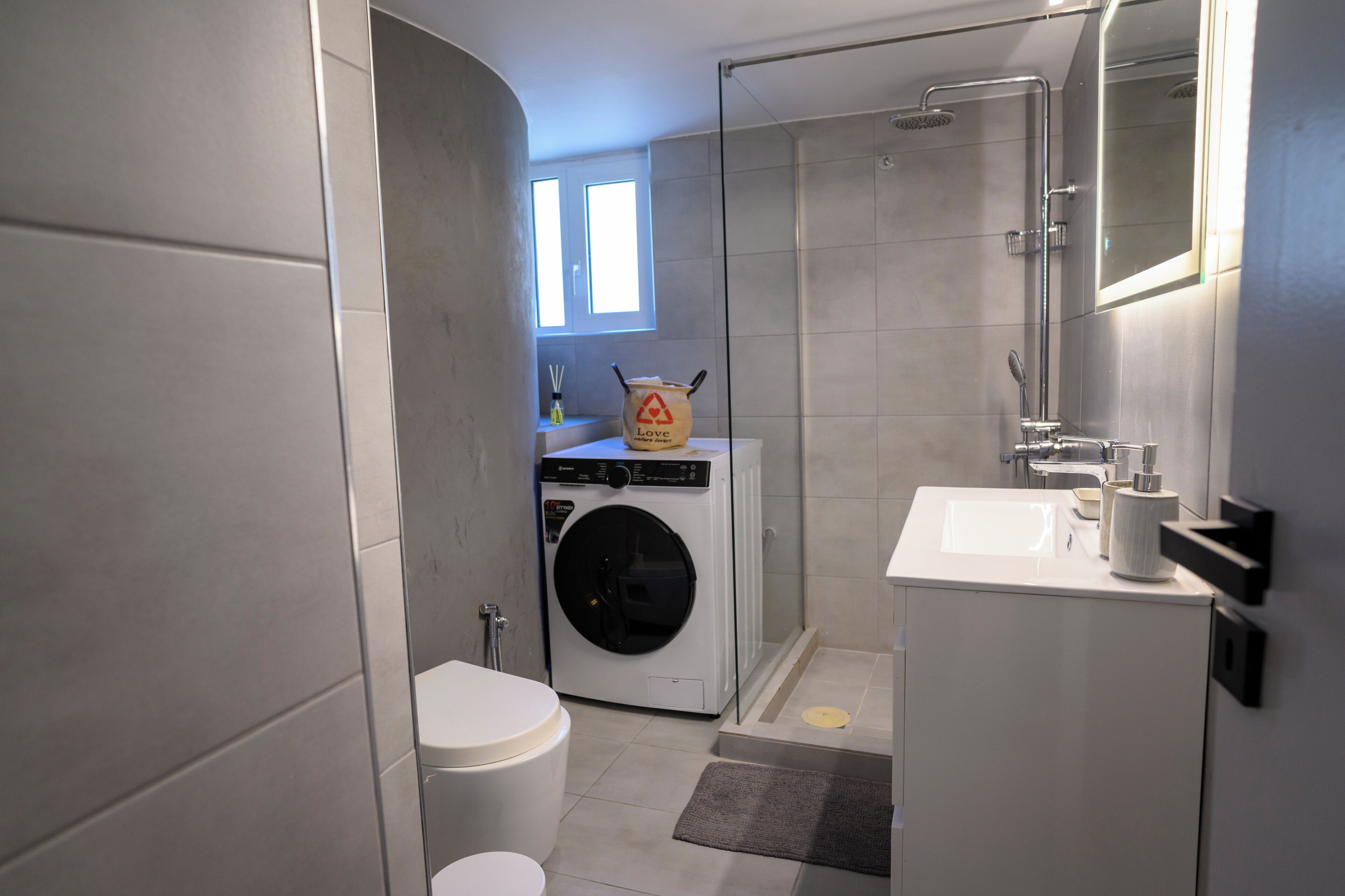 A modern bathroom with a washing machine, toilet, sink, and shower.