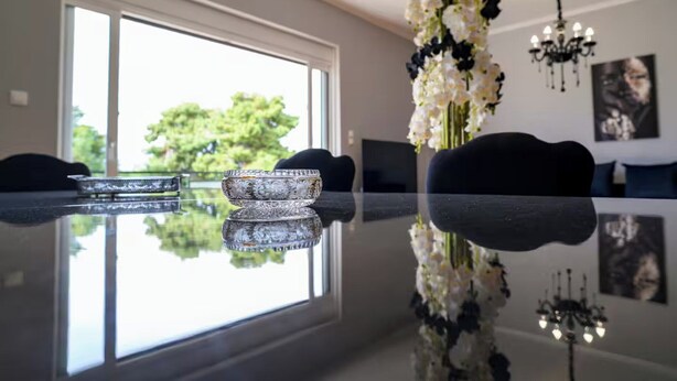 A modern living room with a glass-top table, a vase of flowers, and a chandelier.