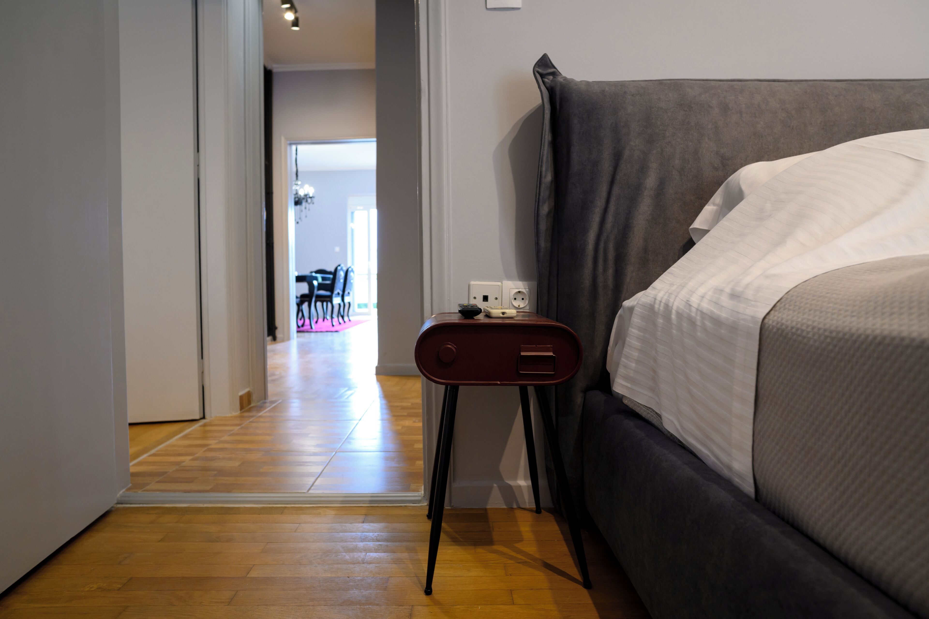 A hotel room with a bed, a bedside table, and a wooden floor.