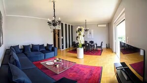 A modern living room with a sectional sofa, a glass coffee table, a dining area with a red rug, and a chandelier.