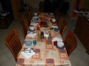 Une table à manger dressée avec des assiettes, des bols, des verres et des couverts, entourée de chaises en bois.