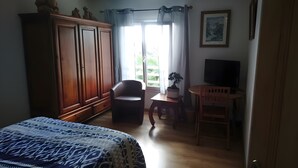 Ein Schlafzimmer mit einem Bett, einem Kleiderschrank, einem Sessel, einem kleinen Tisch mit Pflanze und einem Fernseher.