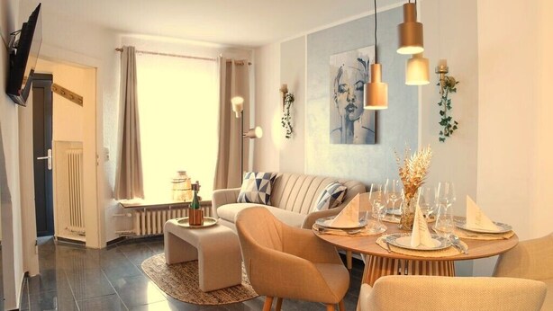 Un salon moderne avec un canapé, une table à manger pour quatre personnes et un téléviseur fixé au mur.
