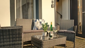 Un coin salon extérieur en osier, avec une table en verre, deux chaises, un canapé et une plante en pot.