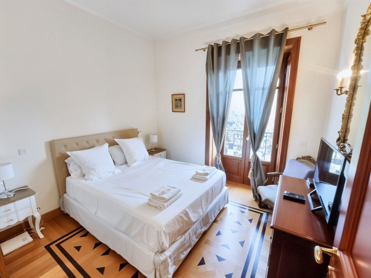 A hotel room with a bed, bedside table, lamp, TV, and a view of the outdoors.