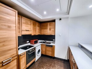 A compact kitchen with wooden cabinets, a washing machine, a microwave, and a sink. - 14494222 FRGK OXFORD Palace Park (Cannes)