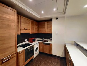 A kitchen with wooden cabinets, a microwave, a washing machine, and a sink. - FRGK OXFORD palace park (Cannes)