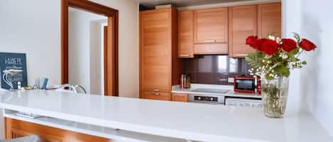 Una cocina moderna con armarios de madera, encimera blanca y un jarrón con flores rojas.