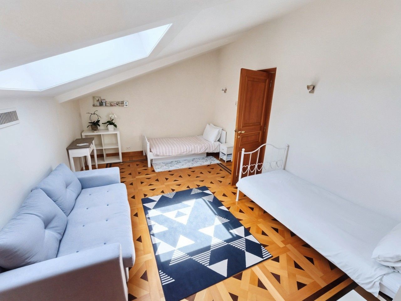 A compact room with a loft bed, a sofa, a small table, and a patterned rug.