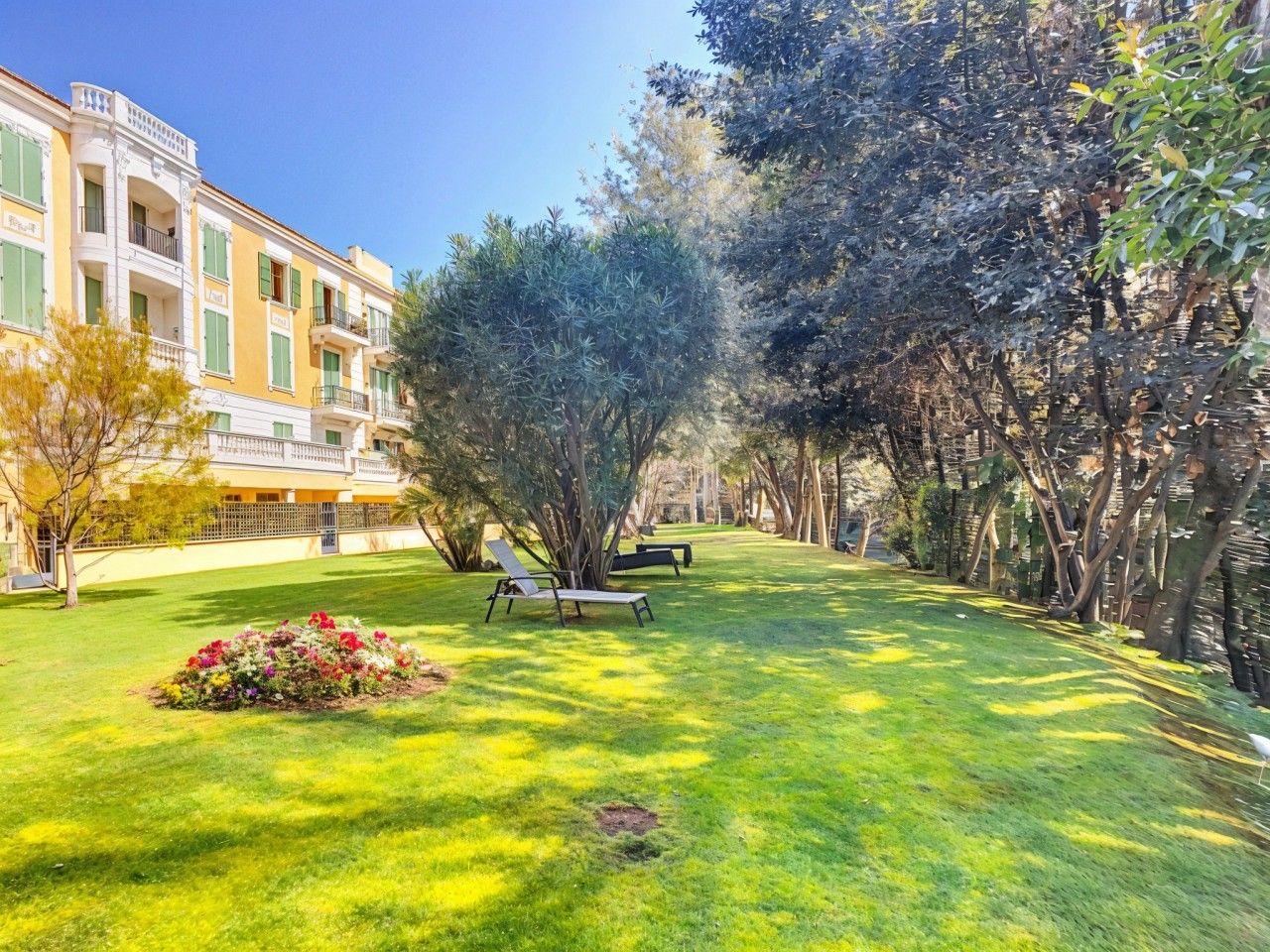 A courtyard with a lawn, two lounge chairs, and a building with balconies.