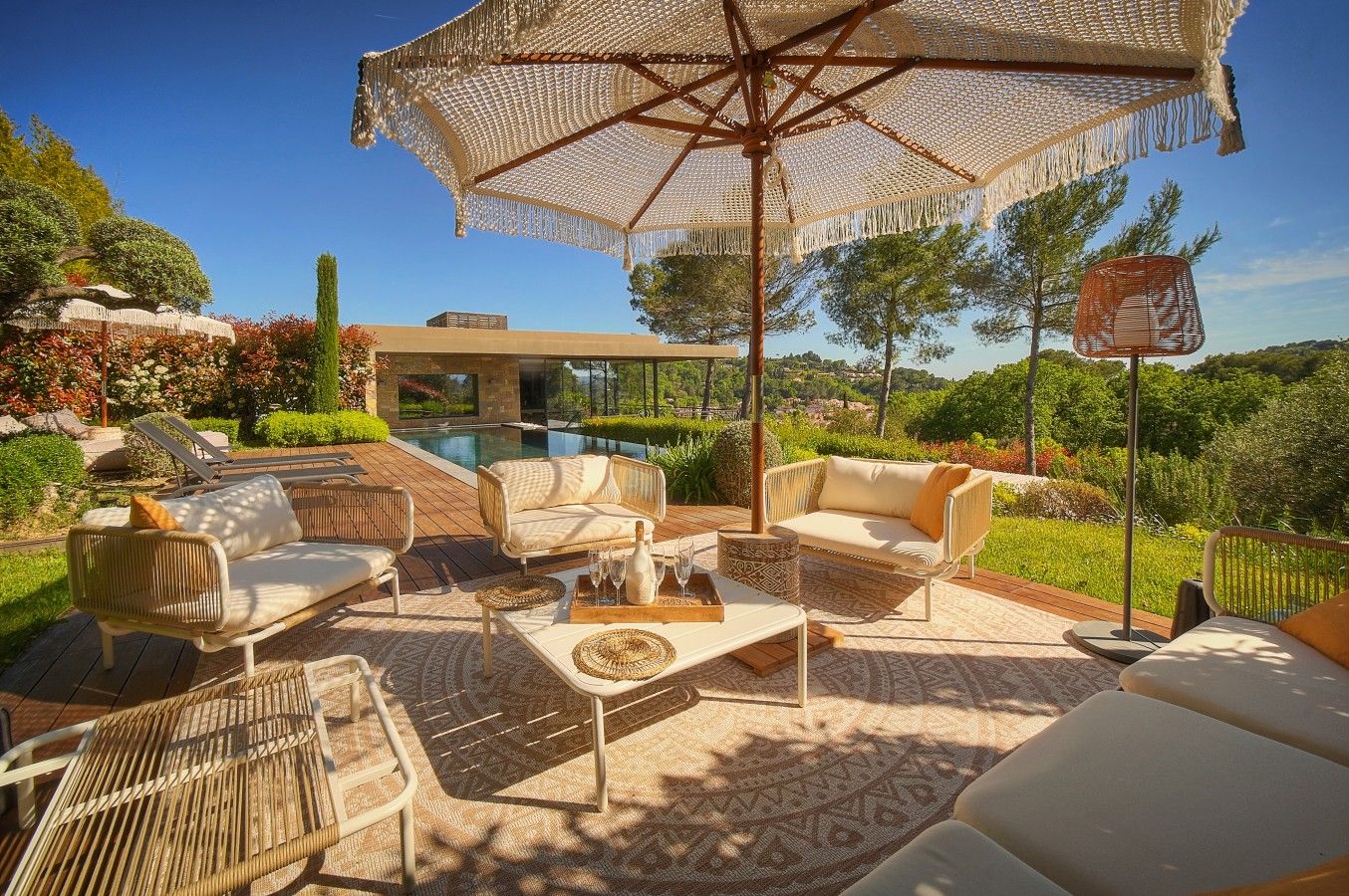 A poolside area with outdoor furniture, a large umbrella, and a view of a modern building and landscape.