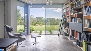 Ein modernes Zimmer mit einer großen Bücherwand, einem Essbereich und Blick auf einen Garten durch Glastüren.