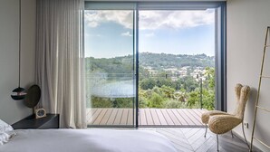 Ein Schlafzimmer mit einer großen Schiebeglasdoor zum Balkon mit Blick auf eine hügelige Landschaft.
