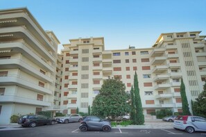 Ein mehrstöckiges Wohnhaus mit Balkonen, geparkten Autos und blauem Himmel.
