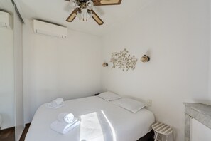 Habitación de hotel con cama, ventilador de techo, aire acondicionado de pared, un adorno en la pared y una mesita de noche pequeña.