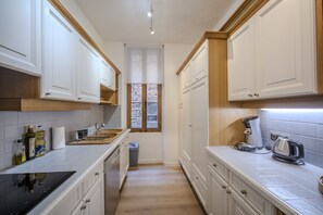 A narrow kitchen with white cabinets, a black stove, and a coffee maker. - Frgk Suquet Olivier 2-Bedroom Charming Apartment with Ultra-Fast Wi-Fi (Cannes)