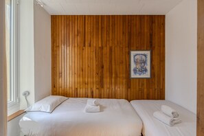 Una habitación con un panel de madera en la pared, dos camas con sábanas blancas y un cuadro enmarcado.