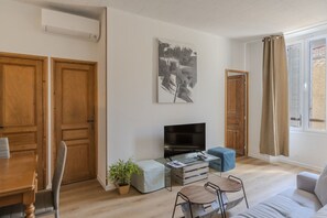 Sala de estar con televisor, puertas de madera, una planta y una ventana con cortinas.