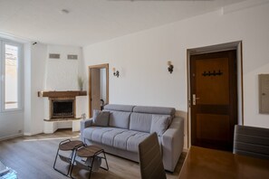 A living room with a sofa, a fireplace, a dining table, and a door. - Frgk Suquet Olivier 2-Bedroom Charming Apartment with Ultra-Fast Wi-Fi (Cannes)