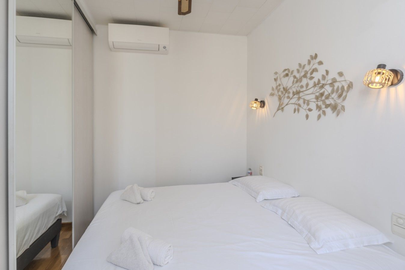 Een hotelkamer met een bed, een wandairconditioner en een decoratieve wandlamp.