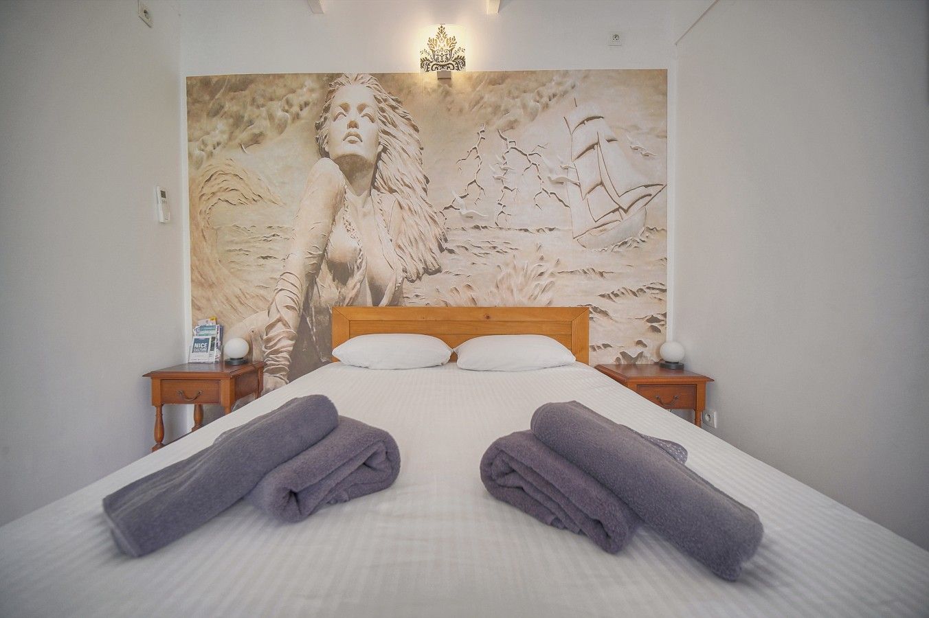 A hotel room with a large bed, two nightstands, and a wall mural.
