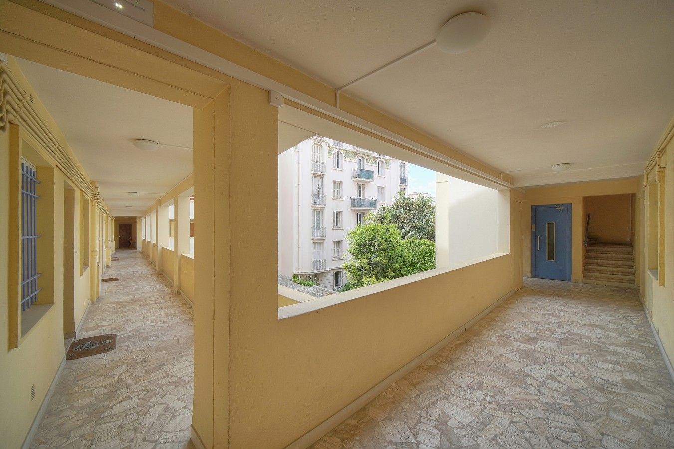 A corridor with a window view of a building and a blue door.