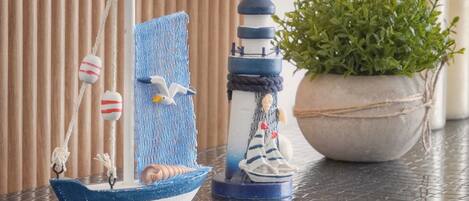 Un petit voilier, un phare et une plante en pot, le tout posé sur une surface carrelée.