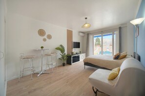 Habitación de hotel moderna con cama, escritorio, dos taburetes de bar, televisor y ventana grande con vistas.