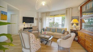 Ein Wohnzimmer mit einer Couch, Sesseln, einem Fernseher, einer Lampe und einem Holzschrank.