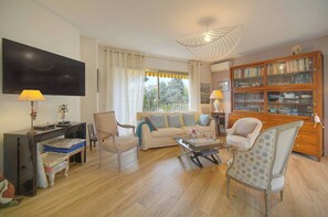 Una sala de estar con un sofá, sillas, un televisor, una estantería y una ventana con cortinas.