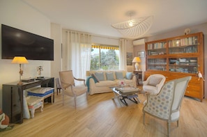 Ein Wohnzimmer mit Sofa, Sesseln, einem Couchtisch, einem Fernseher und einem Bücherregal.