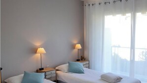 Ein Hotelzimmer mit zwei Betten, jeweils mit Kissen und Lampe ausgestattet. Ein großes Fenster mit Vorhängen ist vorhanden.