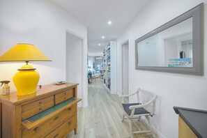 A hallway with a wooden dresser, a yellow lamp, a white chair, and a large mirror on the wall. - 10046194 FRGK `Prince of Wales Garden Terrace` (Cannes)