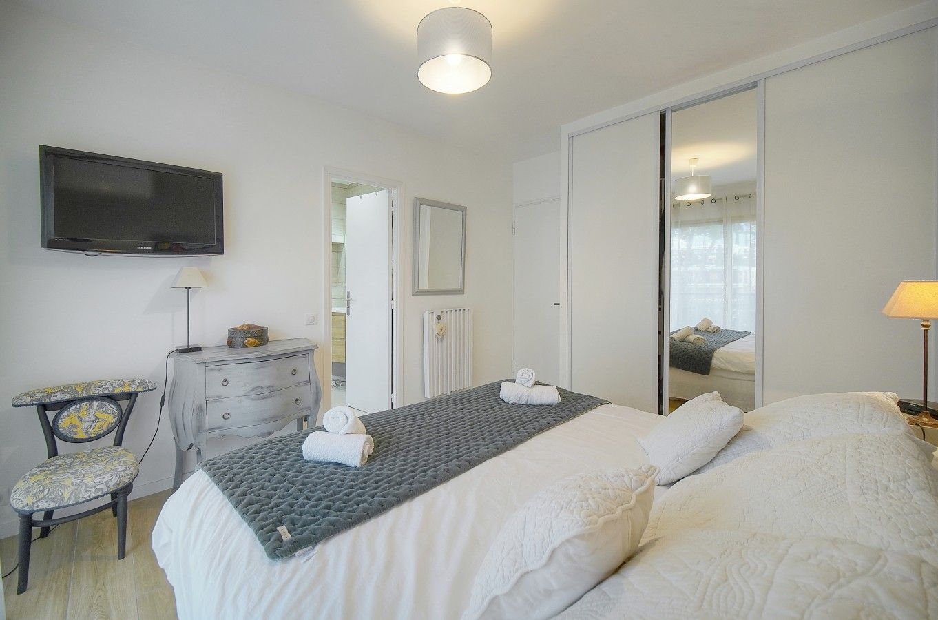 A bedroom with a bed, a dresser, a television, and a mirror.