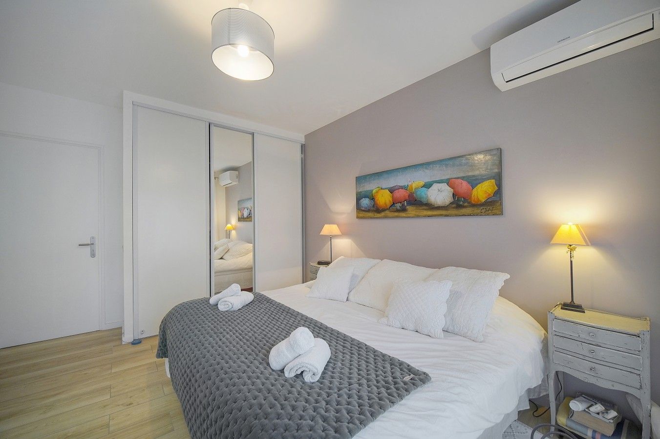 Une chambre d’hôtel avec un lit, des lampes de chevet, un tableau et un appareil de climatisation.