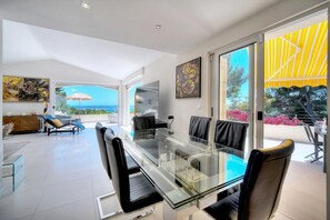 A modern dining area with a glass table and chairs, a sofa, and a view of the outdoors. - Four-bedroom home in France, Vallauris (Vallauris)