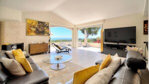 A modern living room with a sofa, coffee table, TV, and a balcony with a view. - FRGK Dream Villa with Sea View Overlooking Cap d (Vallauris)