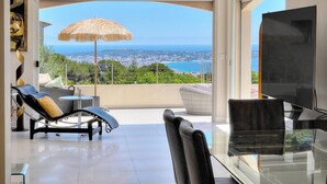 A balcony with a view of the sea, a lounge chair, a glass table, and a TV. - FRGK Dream Villa with Sea View Overlooking Cap d (Vallauris)