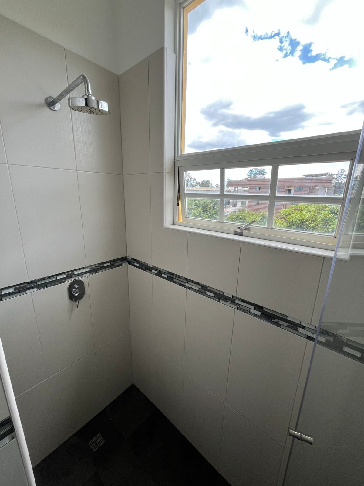 Un baño con ducha, ventana y vistas a edificios.