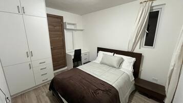 A bedroom with a bed, wardrobe, desk, chair, and a window with curtains.