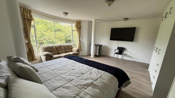 A bedroom with a large bed, a sofa, a TV, and a wardrobe. - Hotel Arupo Residence Aeropuerto (Tababela)