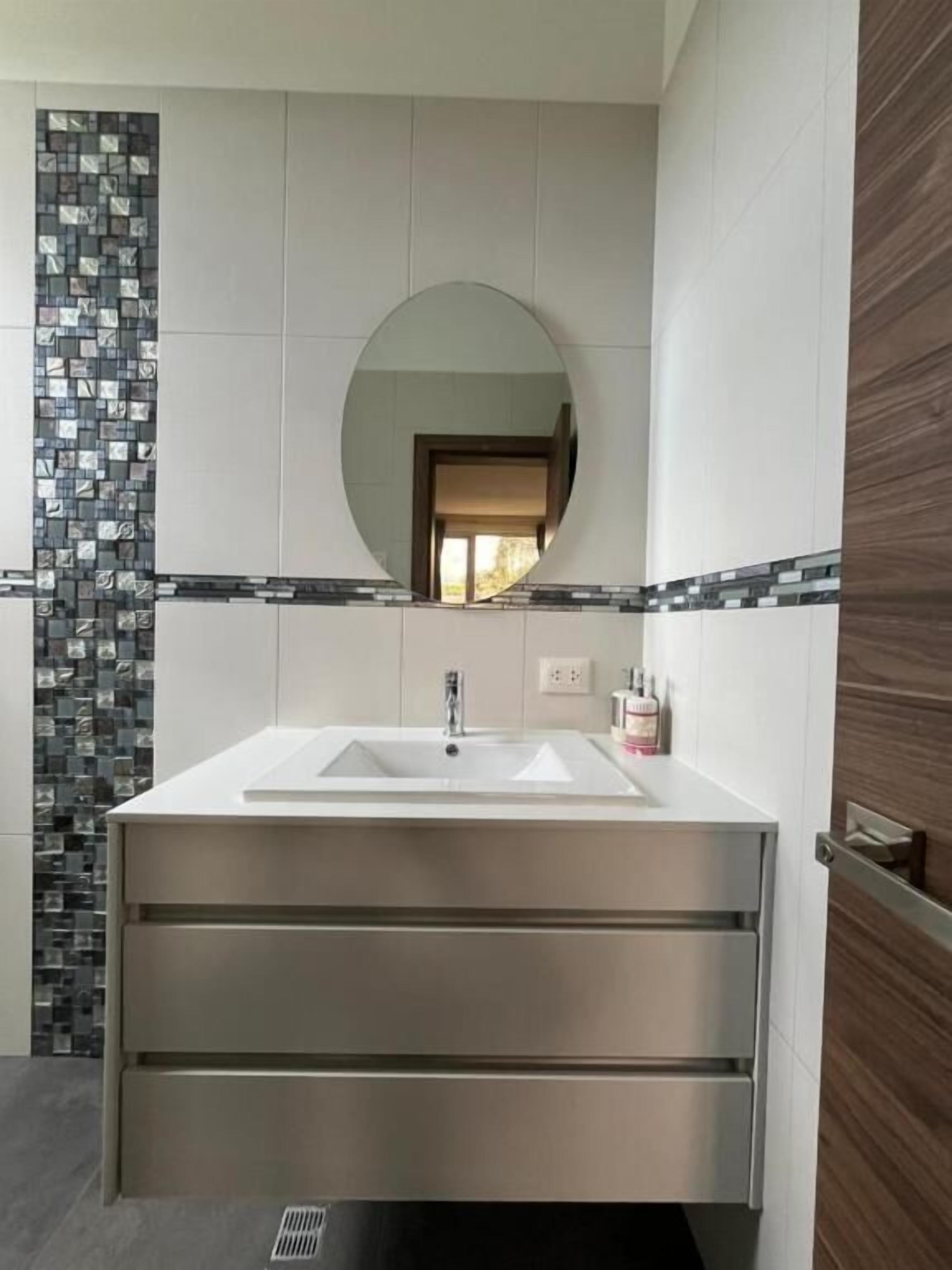A bathroom with a rectangular sink, a mirror, and a tiled wall.