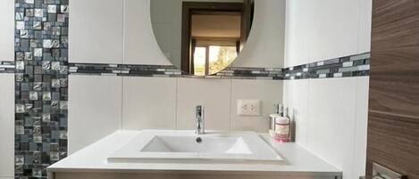 A bathroom with a rectangular sink, a mirror, and a tiled wall.