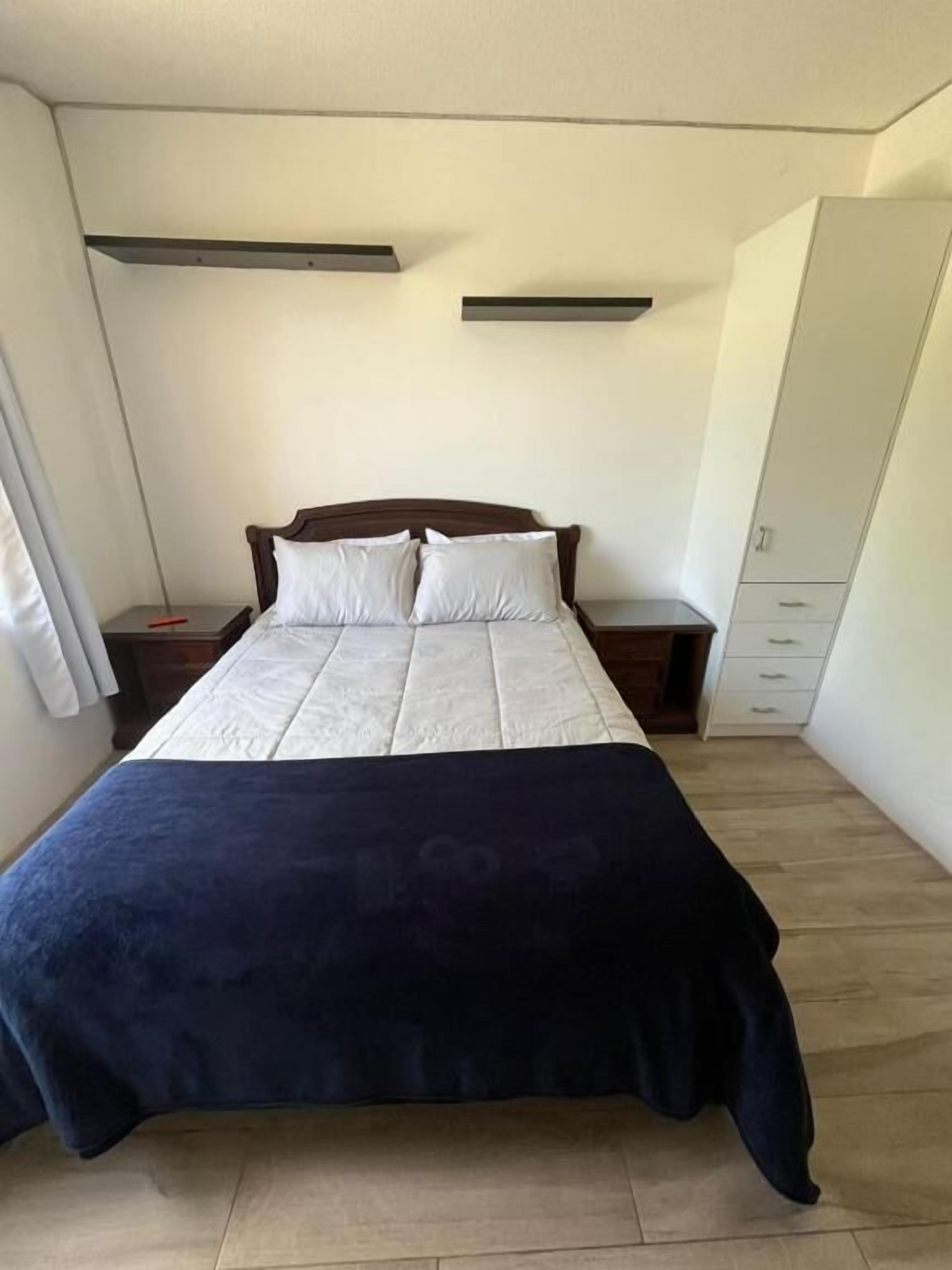 Un dormitorio con cama, mesitas de noche, armario y ventana.
