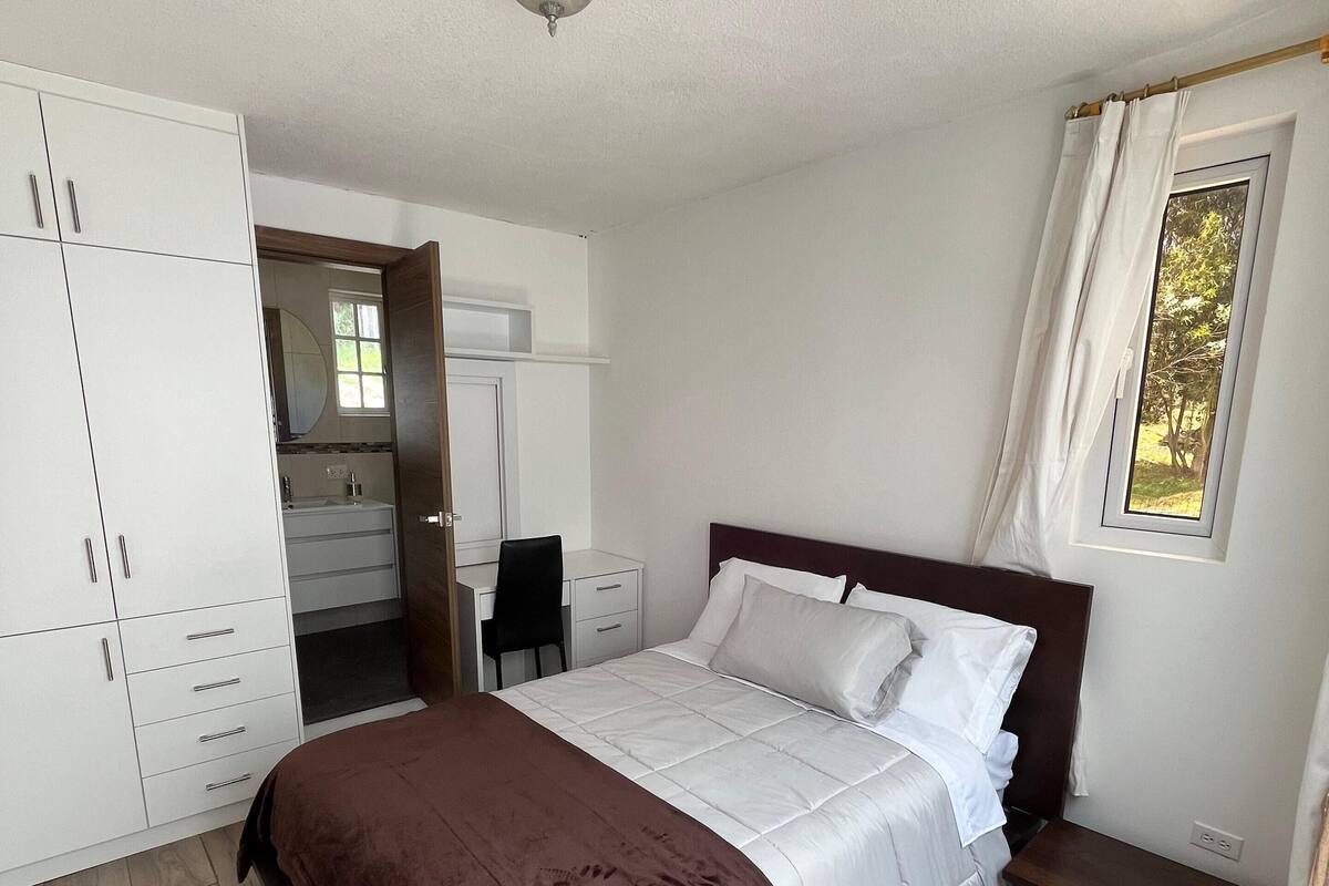 Ein Schlafzimmer mit Bett, Kleiderschrank, Schreibtisch und einem Fenster.