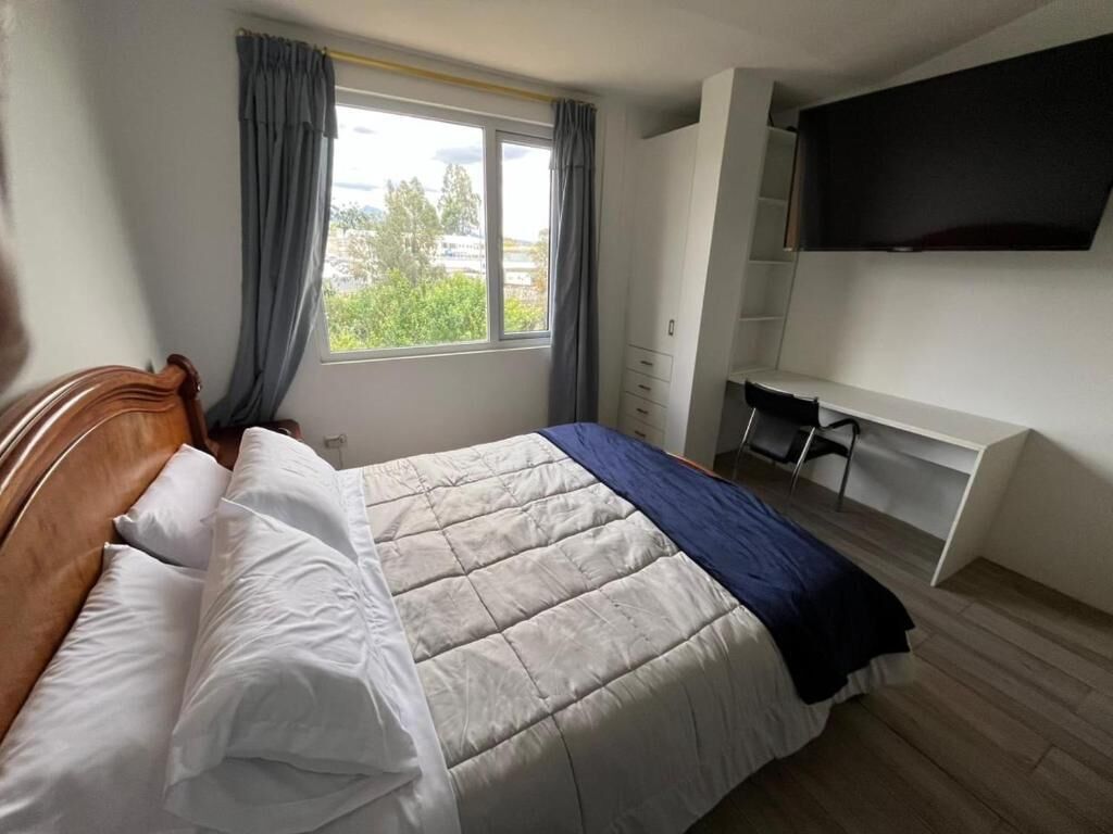 A bedroom with a bed, a desk, and a TV.