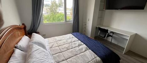 A bedroom with a bed, a desk, and a TV.