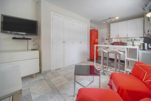 Ein kompakter Wohnraum mit Fernseher, Küchenzeile und Essecke mit Barhocker.