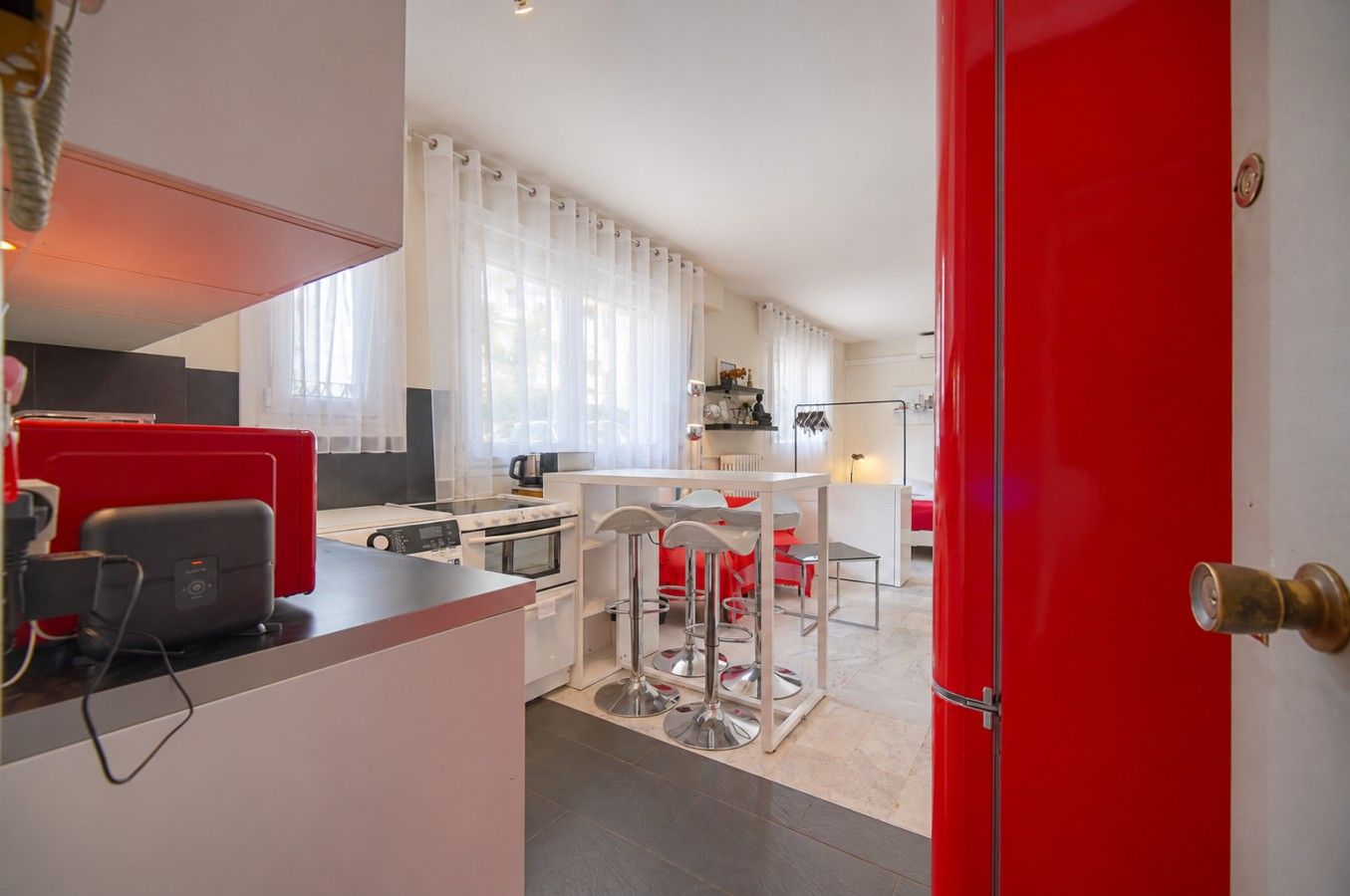 Una cocina moderna con una paleta de colores rojo y blanco, un comedor con sillas rojas y una puerta visible.