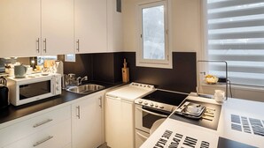 A compact kitchen with white cabinets, a microwave, a stove, and a sink. - SURCOUF (Cannes)
